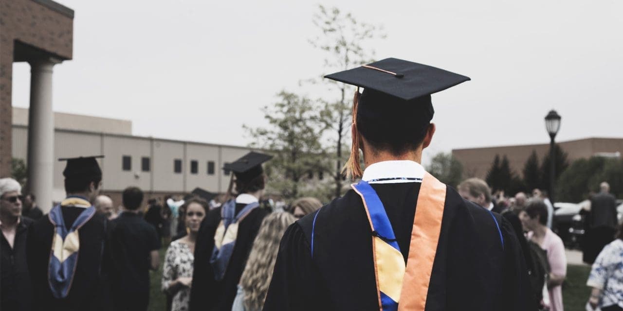 focus back of a man wearing his graduation gown and cap amidst graduation crowd