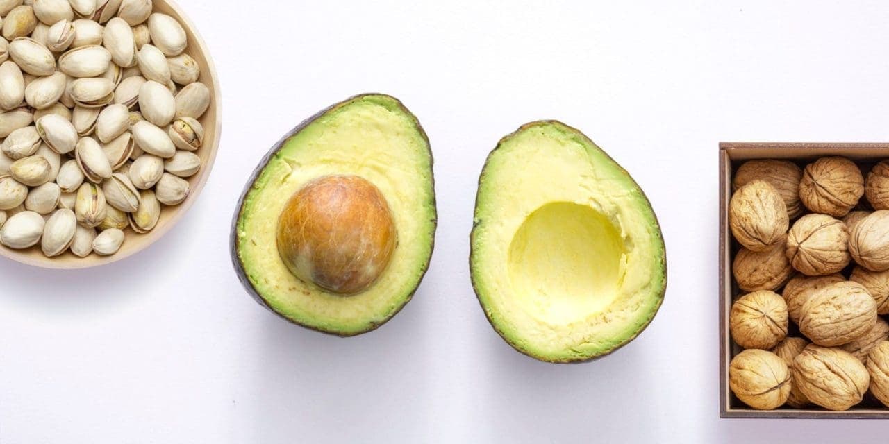 bowl of pistachio nuts on the leaf, sliced avocado on the center and walnuts on a squared wooden container